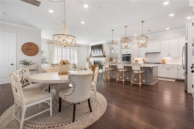 dining area with a notable chandelier, recessed lighting, a fireplace, dark wood finished floors, and crown molding