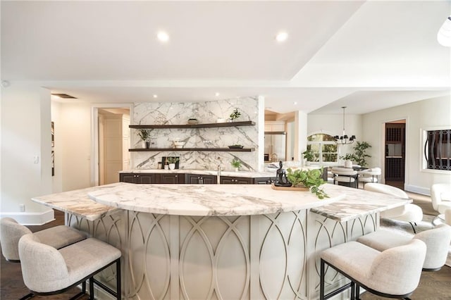 bar with an inviting chandelier, wood-type flooring, and light stone counters