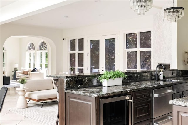 bar with dark brown cabinets, wine cooler, decorative light fixtures, dark stone countertops, and stainless steel dishwasher