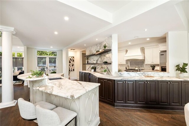 kitchen with dark wood-type flooring, a kitchen bar, custom exhaust hood, dark brown cabinetry, and sink