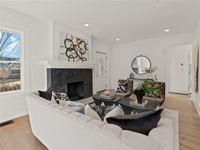 living room with a high end fireplace, light wood-type flooring, and a wealth of natural light