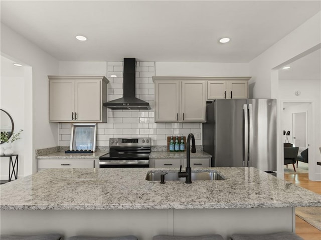 kitchen featuring sink, wall chimney exhaust hood, stainless steel appliances, light stone counters, and a kitchen bar