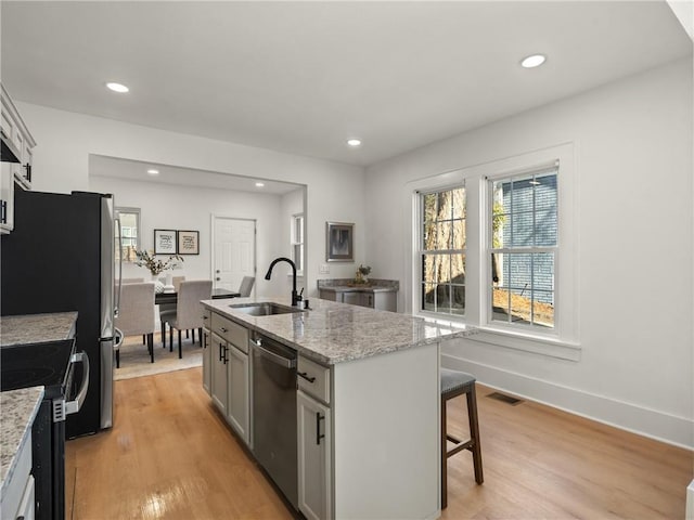 kitchen featuring sink, stainless steel appliances, light stone counters, an island with sink, and light wood-type flooring