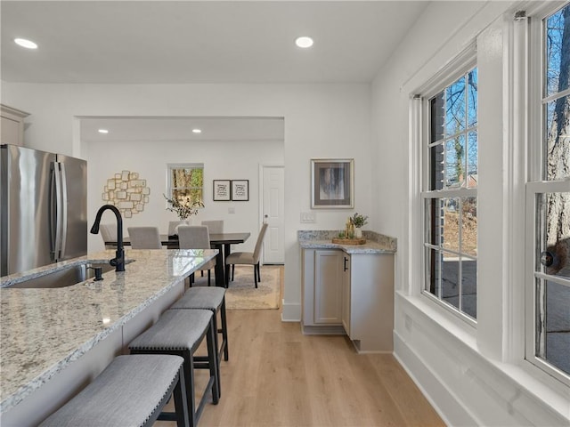 kitchen featuring a breakfast bar, stainless steel fridge, light stone countertops, and light hardwood / wood-style flooring