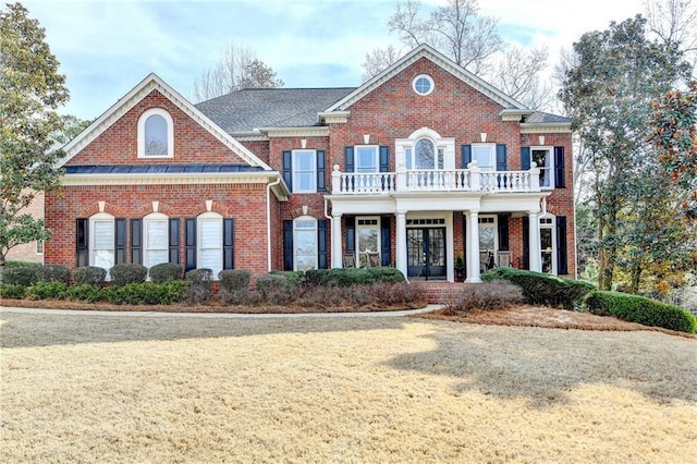 colonial home with a balcony, brick siding, and french doors