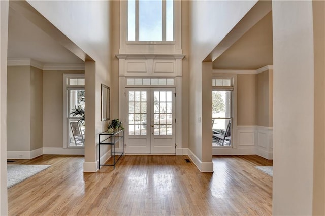 entryway featuring ornamental molding, light wood-style floors, a high ceiling, and a decorative wall