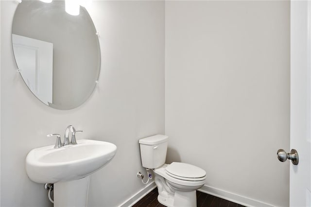 bathroom with toilet, a sink, baseboards, and wood finished floors