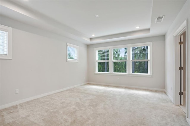 spare room with light carpet, baseboards, visible vents, a tray ceiling, and recessed lighting