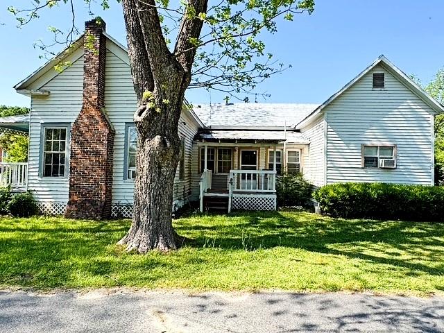 view of front of house featuring a chimney, a porch, and a front lawn