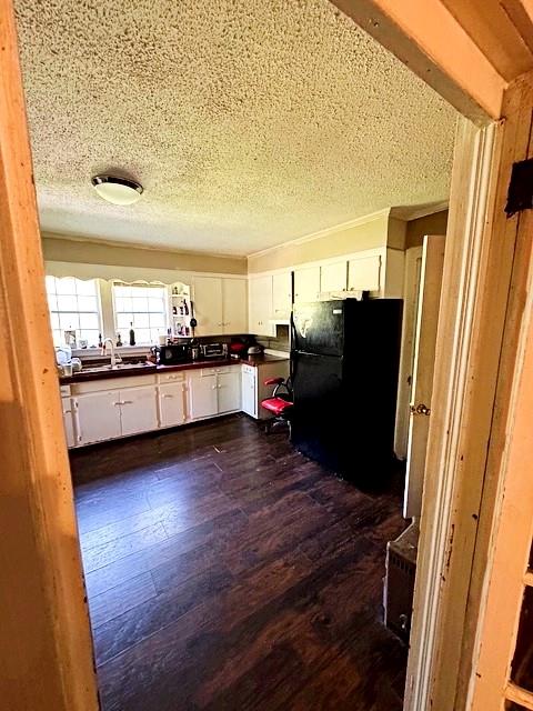 kitchen with dark wood-style flooring, a textured ceiling, dark countertops, freestanding refrigerator, and white cabinetry