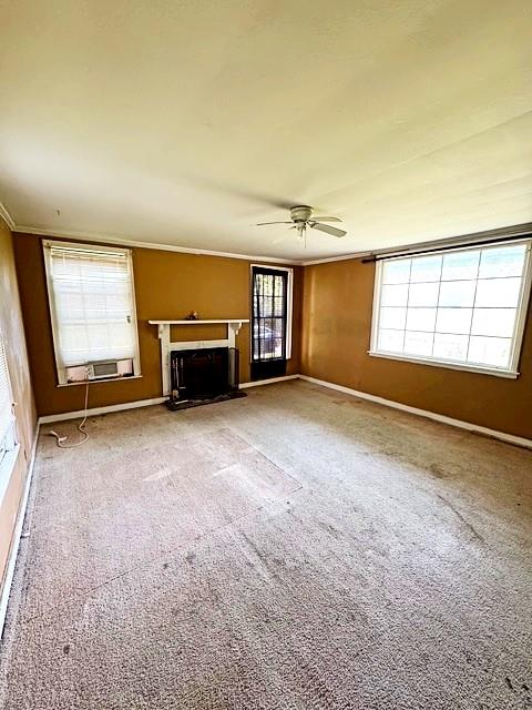 unfurnished living room featuring ceiling fan, a fireplace, baseboards, ornamental molding, and carpet