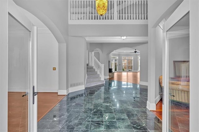 entrance foyer with arched walkways, baseboards, a ceiling fan, and a towering ceiling