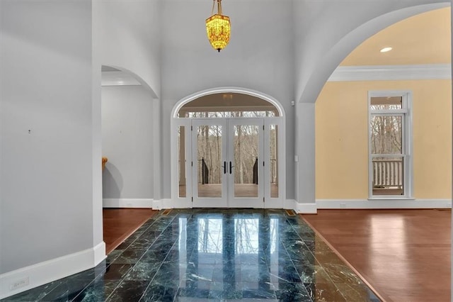 entrance foyer with arched walkways, marble finish floor, french doors, and baseboards