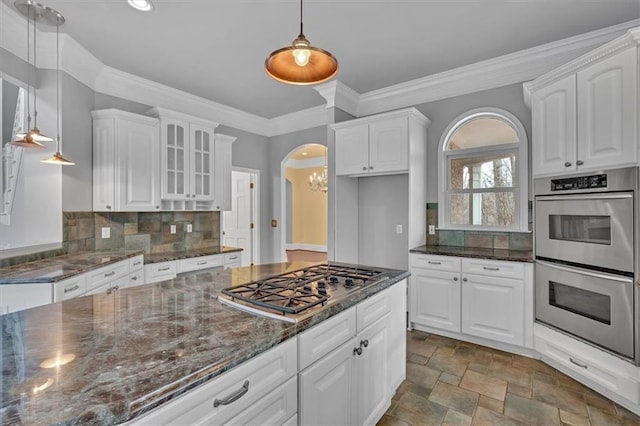 kitchen featuring arched walkways, appliances with stainless steel finishes, white cabinetry, and glass insert cabinets