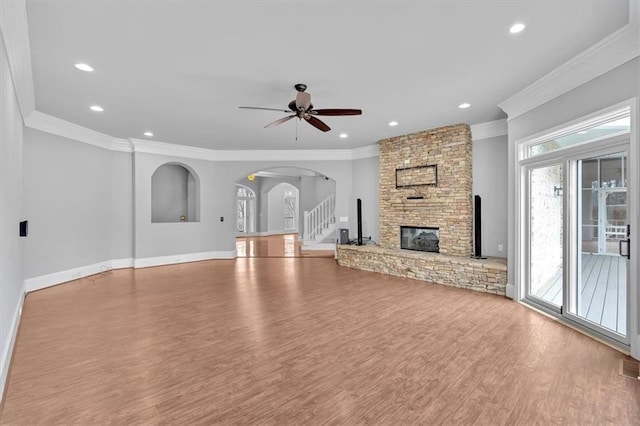 unfurnished living room with wood finished floors, arched walkways, a fireplace, baseboards, and ceiling fan