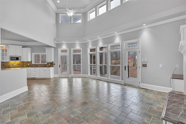 unfurnished living room with ornamental molding, a ceiling fan, stone finish flooring, recessed lighting, and baseboards