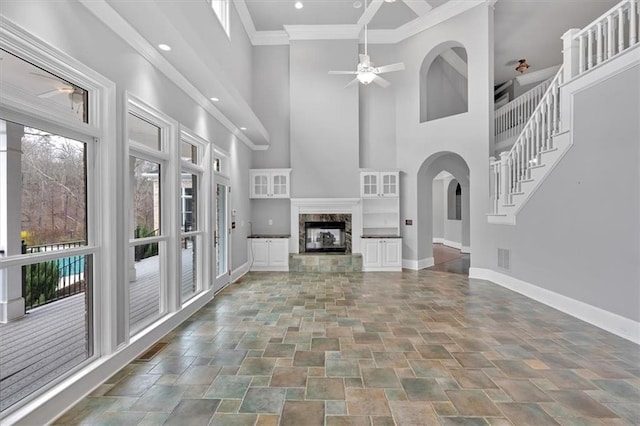 unfurnished living room with a ceiling fan, a high end fireplace, crown molding, baseboards, and stairs