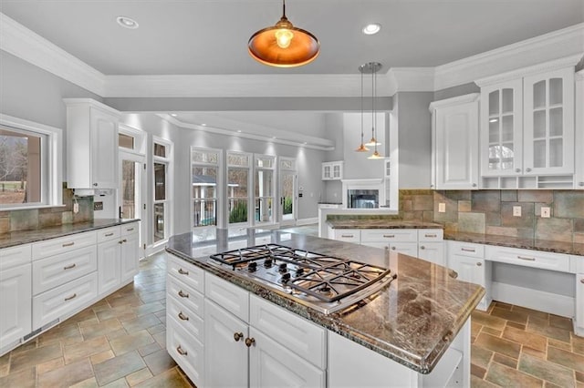 kitchen with ornamental molding, stone tile flooring, stainless steel gas stovetop, white cabinets, and glass insert cabinets