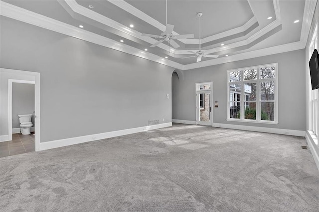 unfurnished living room with crown molding, carpet, arched walkways, and a tray ceiling