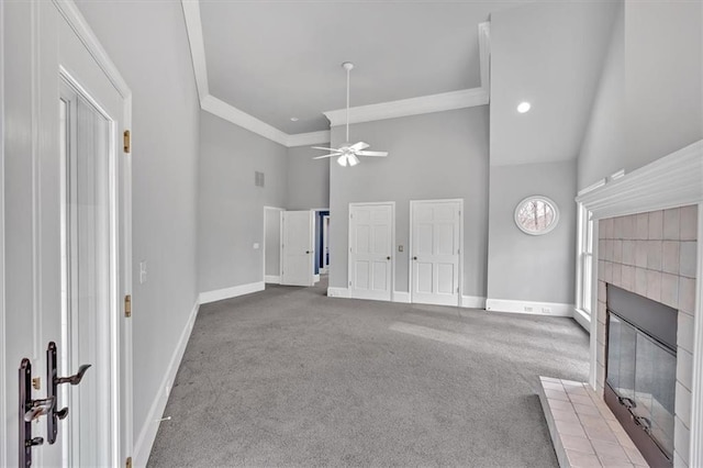 carpeted living room featuring baseboards, a tiled fireplace, a ceiling fan, and crown molding