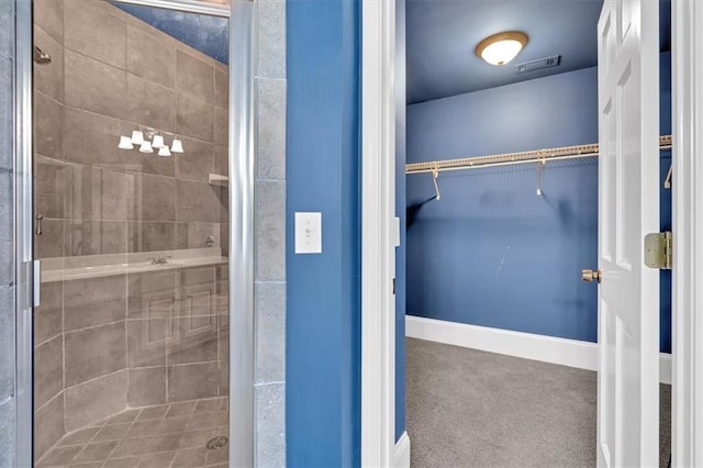 full bathroom with visible vents, a shower stall, a walk in closet, and baseboards