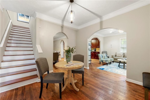 dining room featuring arched walkways, wood finished floors, baseboards, crown molding, and stairs