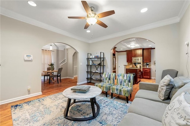living area with arched walkways, light wood-type flooring, a ceiling fan, crown molding, and recessed lighting