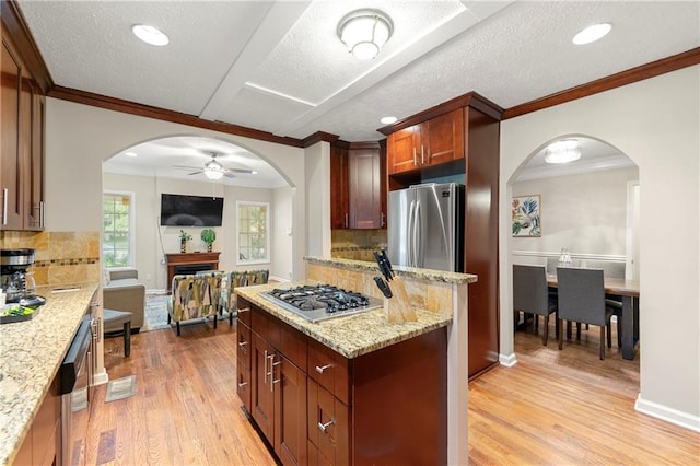kitchen with appliances with stainless steel finishes, arched walkways, ceiling fan, light wood-style floors, and ornamental molding