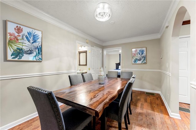 dining room featuring arched walkways, wood finished floors, crown molding, baseboards, and a textured ceiling