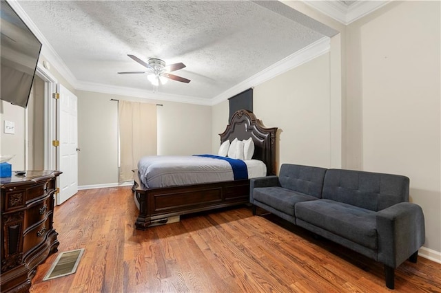 bedroom with wood finished floors, a textured ceiling, crown molding, a ceiling fan, and baseboards