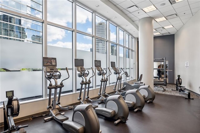 workout area with a towering ceiling, a paneled ceiling, baseboards, and expansive windows