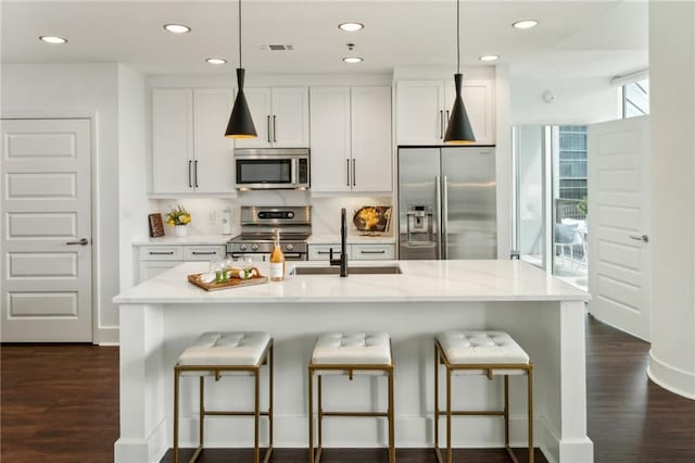 kitchen featuring dark wood finished floors, appliances with stainless steel finishes, a kitchen breakfast bar, white cabinetry, and a sink