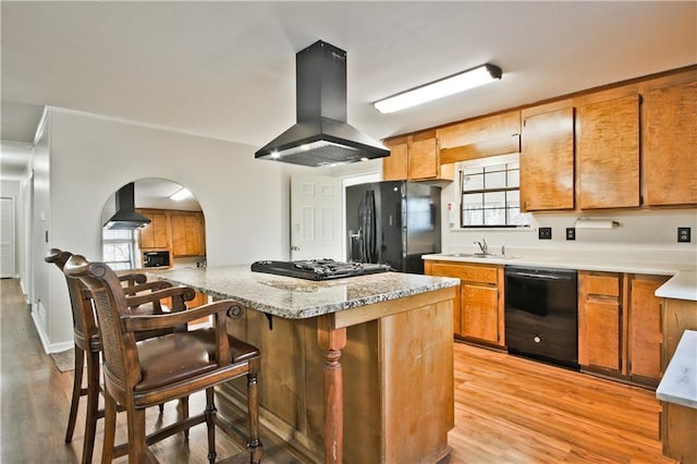 kitchen featuring black appliances, wall chimney exhaust hood, a kitchen breakfast bar, island range hood, and light hardwood / wood-style flooring