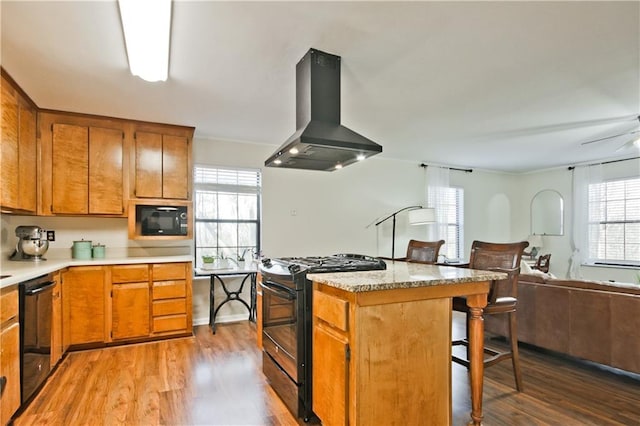 kitchen with black appliances, island exhaust hood, light hardwood / wood-style flooring, plenty of natural light, and a breakfast bar area