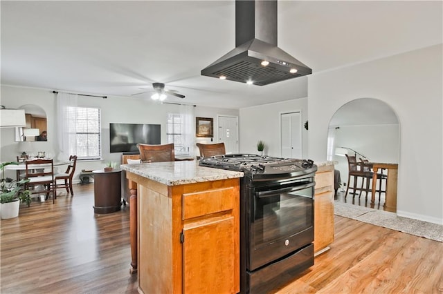 kitchen featuring a kitchen island, light hardwood / wood-style floors, black range with gas cooktop, island range hood, and ceiling fan