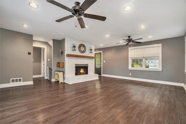 unfurnished living room featuring dark wood-type flooring, a large fireplace, and ceiling fan