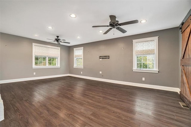 empty room featuring dark wood-type flooring, ceiling fan, a barn door, and a wealth of natural light