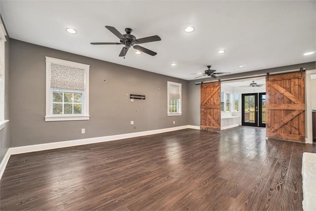 unfurnished living room with a barn door, dark wood-type flooring, and ceiling fan