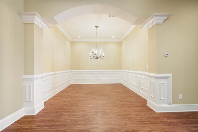 unfurnished dining area with a notable chandelier, crown molding, arched walkways, and wood finished floors