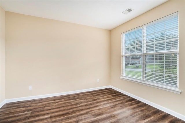 empty room featuring baseboards, visible vents, and dark wood-style flooring