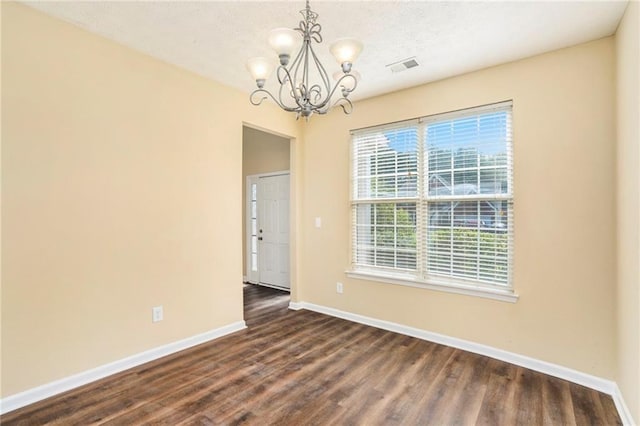 empty room with dark wood-style floors, visible vents, baseboards, and a chandelier