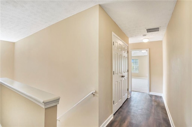 hallway with dark wood-style floors, visible vents, a textured ceiling, an upstairs landing, and baseboards