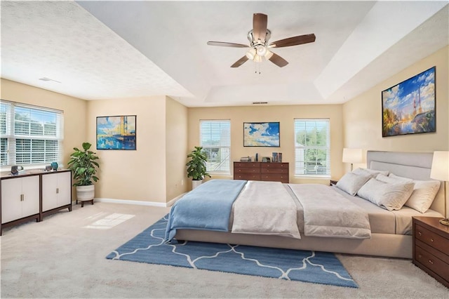 bedroom featuring light carpet, baseboards, a raised ceiling, and a ceiling fan