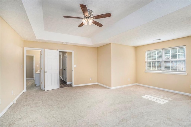 unfurnished room featuring light carpet, baseboards, a raised ceiling, and a textured ceiling