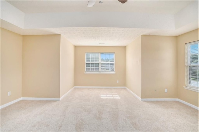 empty room featuring a textured ceiling, light colored carpet, and baseboards