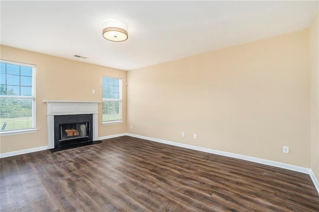 unfurnished living room featuring a fireplace with flush hearth, dark wood finished floors, visible vents, and baseboards