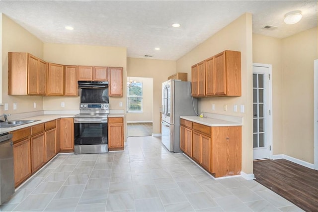 kitchen featuring baseboards, appliances with stainless steel finishes, light countertops, under cabinet range hood, and a sink