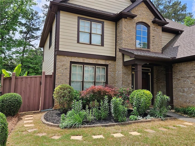 view of home's exterior featuring fence, a shingled roof, and brick siding