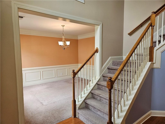 staircase with ornamental molding, an inviting chandelier, and wood finished floors