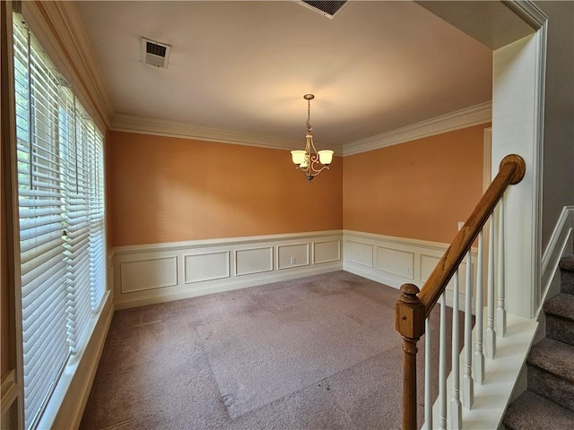 carpeted empty room featuring crown molding, a chandelier, visible vents, and a decorative wall